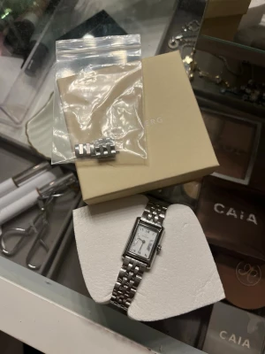 Silverfärgad klocka från Mockberg - Stilren klocka från Mockberg med rektangulär vit urtavla och silverfärgat armband i metall. Klockan har minimalistisk design och kommer med extra länkar för justering av storlek. Perfekt accessoar för en clean look.