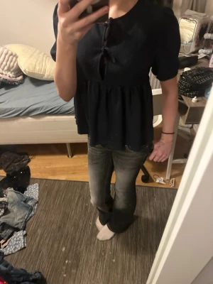 Svart topp med knyt och puffärm - Säljer en svart topp med puffärmar och två knyt framtill. Toppen har en lös passform och rund halsringning. Perfekt för dig som gillar en enkel men ändå söt stil. Materialet känns mjukt och toppen har en lätt volang nedtill.