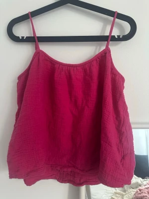 Rosa linnetopp från H&M - Säljer en rosa linnetopp från H&M med tunna axelband och lös passform. Toppen är tillverkad i ett mjukt, strukturerat bomullstyg som känns luftigt och perfekt för varma dagar. Enkel och stilren design som är lätt att matcha.