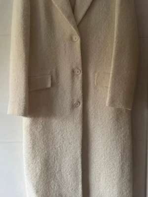 Ny. Krämvit bouclé kappa från Zara - Stilren krämvit kappa från Zara i bouclé-liknande material. Kappan har tre knappar framtill, klassisk krage och två fickor med lock. Rak passform och helfodrad för extra komfort. Perfekt för dig som gillar minimalistisk och trendig stil. Ull blandad med bomull. Impuls köp, kom aldrig till användning. Kostade 1199kr, nu 750. Ej prutbär.