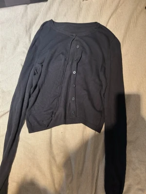Mörkblå tunn kofta med knappar - Skulle säga xs/s. En enkel och stilren mörkblå kofta med rund halsringning och knäppning framtill. Koftan är tunnstickad och har ribbade muddar vid ärmslut och nederkant. Perfekt att slänga över en t-shirt eller linne för en avslappnad look.