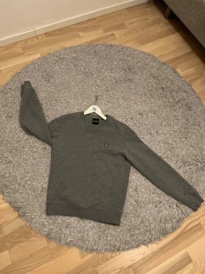 Grå sweatshirt från Lyle & Scott - En stilren grå sweatshirt från Lyle & Scott. Perfekt för våren. Tröjan är S, 