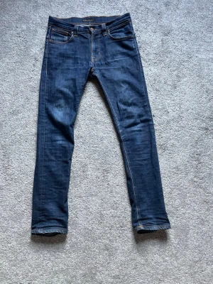 Mörkblå jeans från Nudie Jeans - Märke: nudie jeans.                                                Storlek 32/32.                                                             Modell: tape Ted.                                                       Färg: marinblå med fet wash.                                  Sliten i skrevet