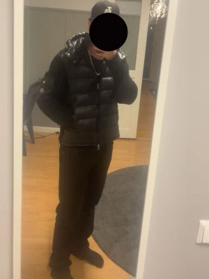 INTRESSEKOLL  på en cardigan från Moncler - Säljer en svart dunväst från Moncler med hög krage och dragkedja framtill. Västen har en glansig finish, två fickor med dragkedja och Moncler-logga på axeln. Perfekt för lager-på-lager och riktigt snygg till streetwear-stilen.