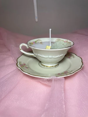 Doftljus i vaniljdoft i en tekopp med fat med blommig design  - Det här ljuset är gjort av återanvändbara material. Tekoppen är köpt secondhand och stearinet är från kyrkor som tänkte slänga det. Det här ljuset har en svag doft utav vanilj, så känsliga även kan använda det. Det här ljuset har även torkade blommor på som dekoration. 