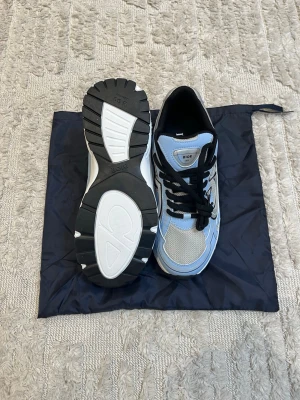 Dior sneakers i blått och vitt - Snygga Dior sneakers i blått, vitt och svart med mesh och läderdetaljer. Skorna har en chunky sula och svarta skosnören. Märket syns tydligt på plösen. Perfekta för dig som vill ha en exklusiv och trendig look.
