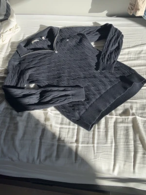 Mörkblå kabelstickad tröja - Mörkblå kabelstickad tröja med halv dragkedja och hög krage. Tröjan har långa ärmar och ribbade muddar vid ärmslut och nederkant. Klassisk och stilren design som passar till mycket. Materialet känns mjukt och bekvämt.