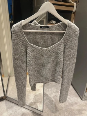 Grå ribbstickad tröja Gina Tricot - Trendig grå ribbstickad tröja från Gina Tricot med bred, fyrkantig urringning och långa ärmar. Tröjan har en croppad passform och ett snyggt mönster framtill. 