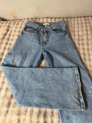 Blå raka jeans från H&M - Säljer ett par klassiska blå raka jeans från H&M i storlek 36. Jeansen har fem fickor, hög midja och är gjorda i ett slitstarkt denimtyg. Perfekta för en avslappnad och trendig look. Passar dig som gillar tidlös stil och enkelhet.