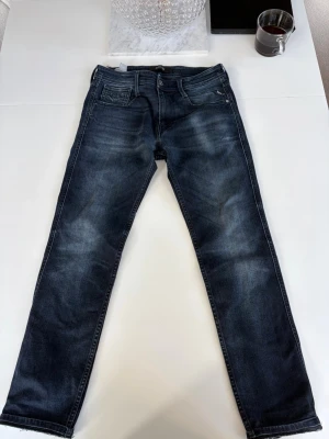 Mörkblå jeans från Replay - Snygga mörkblå jeans från Replay med klassisk femficksdesign och lätt slitna detaljer på låren. Jeansen är i slim fit modell  och är tillverkade i ett mjukt denimtyg som ger en bekväm passform. Perfekta för en avslappnad och trendig look.