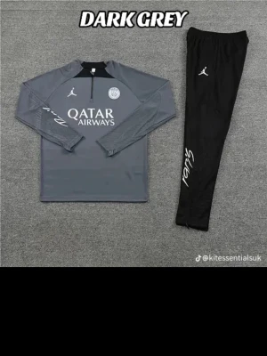 Mörkgrå PSG träningsset Jordan - Snyggt mörkgrått PSG träningsset från Jordan med långärmad tröja och svarta byxor. Tröjan har dragkedja vid halsen, PSG-logga och Qatar Airways-tryck. Byxorna har Jordan-logga och vit text på benet. Perfekt för träning eller chill.