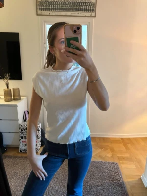 bikbok topp - Säljer en stilren vit ribbad topp med rund halsringning. Toppen är ärmlös och har en rak passform som sitter snyggt till både jeans och kjol. Perfekt för dig som gillar enkla men trendiga plagg.