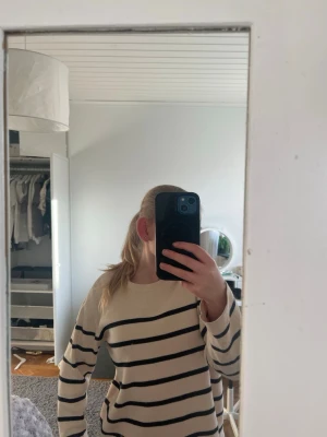 Randig beige stickad tröja - Säljer en beige stickad tröja med svarta horisontella ränder. Tröjan har rund halsringning, långa ärmar och ribbade muddar. Perfekt för dig som gillar klassisk och enkel stil. Materialet känns mjukt och bekvämt.