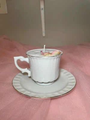 Doftljus i vaniljdoft i en vit tekopp med fat  - Det här ljuset är gjort av återanvändbara material. Tekoppen är köpt secondhand och stearinet är från kyrkor som tänkte slänga det. Det här ljuset har en svag doft utav vanilj, så känsliga även kan använda det. Det här ljuset har även torkade blommor på som dekoration. 