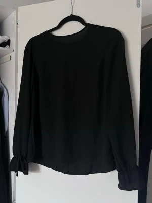 Svart blus med rosett vid ärmarna från Gina Tricot, stl 34 - Stilren svart blus i luftigt material med långa ärmar. Ärmsluten har en söt rosettdetalj. Rund halsringning och rak passform.