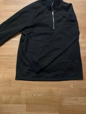 Svart halvzip tröja - Snygg svart långärmad tröja med halvzip och hög krage. Perfekt för lager på lager och enkel att matcha med olika outfits. Tröjan har ribbade muddar vid ärmsluten och en stilren look.