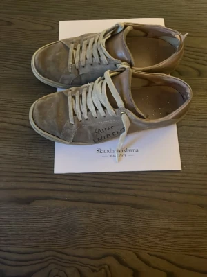 Saint Laurent gråa låga sneakers - Gråa låga sneakers från Saint Laurent med vita snören och klassisk siluett. Ovandelen är i läder med handskriven logga på sidan. Snygg vintagekänsla och neutrala färger som passar till det mesta.