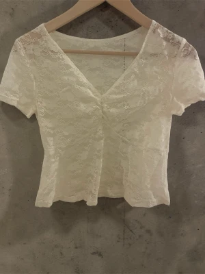 Ljus gul spetsblus med v-ringning - Söt ljus gul blus i spets med korta ärmar och v-ringad hals. Blusen har ett blommigt spetsmönster och lätt figurnära passform. Perfekt att styla med jeans eller kjol för en trendig look.