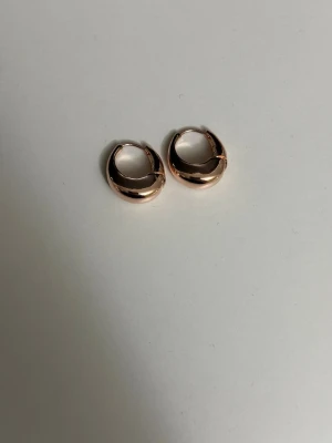 Guldfärgade chunky hoops örhängen - Säljer ett par chunky hoops örhängen i guldfärgad metall. De är runda och har en blank, polerad yta som ger en modern och stilren look. Perfekta för att lyfta vilken outfit som helst.