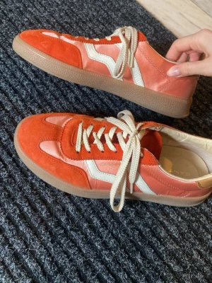 Röda och vita sneakers från Gant - Snygga sneakers från Gant i rött och vitt med beige detaljer. Ovandelen är i mocka och textil, med vita snören och en klassisk gummisula. Perfekt för dig som gillar retrostil och vill sticka ut lite extra.