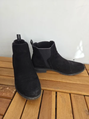 Ankel boots i mocka - Ankel boots i mocka med klassisk resår på sidorna och dragflik bak. Skorna har låg klack och rundad tå.