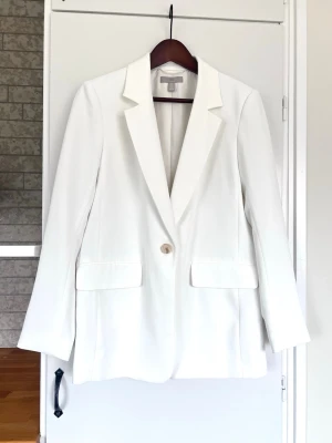 Clean vit kavaj från H&M, storlek S - Snygg vit kavaj från H&M med klassisk krage, en knapp framtill och fyra dekorativa knappar vid ärmslutet. Passar så bra med kostymbyxor eller ett par blå jeans nu till våren! 🌸 Säljer pga att den inte kommer till användning.  True to size. En liten fläck vid vänster ärmslut (knappt synbar) - se sista bilden. Ska tvättas på kemtvätt men den har tvättats i maskin en gång och det gick utmärkt! Använd en gång - originalpris 499.
