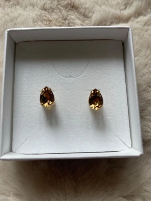 Guldörhängen med bruna stenar - Snygga örhängen från Caroline Svedbom med droppformade, bruna kristaller infattade i guldfärgad metall. Perfekta för dig som vill ha en elegant och stilren accessoar med exklusiv känsla. Levereras i originalask.