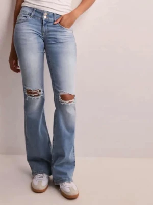 Lågmidjade bootcut jeans med hål - Säljer ett par lowrise ljusblå bootcut jeans med slitna detaljer över knäna och snygg tvätt. Jeansen har klassiska fem fickor, knappgylf och bakfickor med lock och knapp. Perfekta för en avslappnad och trendig look.