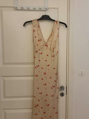 Satinklänning  - Söt gul/champangefärgad långklänning med röda blommor och v-ringning. Klänningen är ärmlös och har omlottdetalj med knyt i midjan. Perfekt för sommarens alla tillfällen och ger en romantisk vibe. Är tyvärr för liten så har ingen bild på