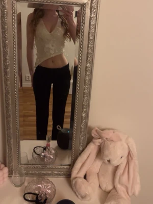 Vit spetsig croppad omlottopp - Säljer en vit croppad omlottopp med spetsdetaljer och v-ringning. Toppen är ärmlös och har en feminin, figurnära passform som passar perfekt till både jeans och kjol. Perfekt för dig som vill ha en söt och trendig topp till sommaren.