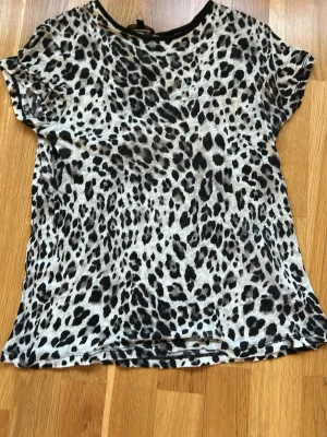 Leopardmönstrad topp Massimo Dutti - Säljer en snygg leopardmönstrad topp från Massimo Dutti i svart och grått. Toppen har korta ärmar och rund halsringning. Perfekt för dig som vill sticka ut lite extra med ett djurmönster. Superlätt och skön att bära.