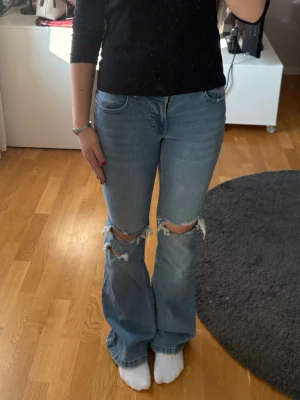 Ljusblå slitna bootcut jeans - Säljer ett par ljusblå bootcut jeans med slitningar över knäna. Även om de är en liten storlek så känns de större än det, jag som är 158 trampar på de där nere, de är också lite stretchiga. Aldrig använda, nypris 900 kr.