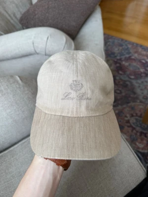 Loro piana linne keps  - Snygg beige keps från Loro Piana i ett luftigt linnematerial. Klassisk sexpanel-design med böjd skärm och diskret broderad logga framtill. Perfekt accessoar för en clean och stilren look.