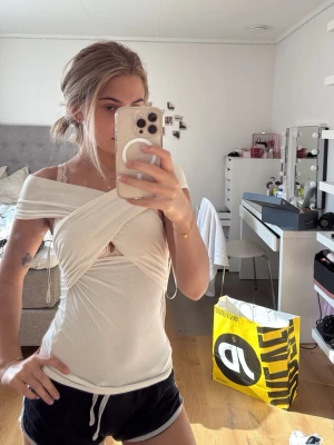 Vit omlott offshoulder topp - Trendig vit omlott topp med offshoulder-design och snörning i sidan. Toppen är tight och har en unik omlottkänsla framtill. Perfekt för dig som vill ha en stilren men ändå cool look.