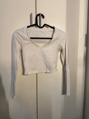 Vit croppad långärmad topp - Snygg vit croppad topp med lång ärm och v-ringad hals. Perfekt att matcha med höga jeans eller kjol för en clean och enkel look. Tillverkad i mjuk bomull som känns skön mot huden.