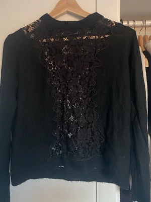 Svart stickad tröja med spets från Zara - Snygg svart stickad tröja från Zara med långärmad design och detaljer i spets framtill och vid axlarna. Tröjan har en rund halsringning och är gjord i ett tunt, lätt material som ger en elegant look. Perfekt för dig som gillar trendiga och feminina plagg.