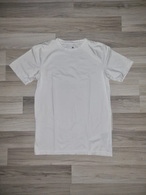 Vit basic t-shirt i bomull - En klassisk vit t-shirt med rund hals och korta ärmar. Tillverkad i mjuk bomull för en skön känsla och enkel stil. Perfekt att matcha med jeans eller shorts för en clean look.