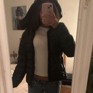 Svart pufferjacka med huva - Säljer en svart pufferjacka med huva. Jackan har quiltad design och dragkedja framtill. Perfekt för kalla dagar och har en modern, boxig passform. Passar dig som vill ha en stilren och enkel vinterjacka.