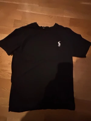 Svart t-shirt från Ralph Lauren - Klassisk svart t-shirt från Ralph Lauren med den ikoniska vita broderade loggan på bröstet. Det är 160-164cm