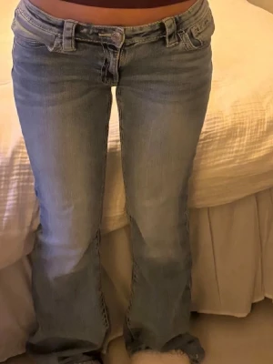 Ljusblå bootcut jeans - Säljer ett par ljusblå bootcut jeans med låg midja och klassisk femficksdesign. Jeansen har slitningar och en tvättad look som ger en avslappnad vibe. Perfekta för dig som gillar retrostil och vill ha ett par sköna jeans till vardags.