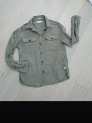 Olivgrön overshirt från Hollister - Snygg olivgrön overshirt från Hollister. Skjortan har lång ärm och en avslappnad passform, perfekt för en chill och stilren look.