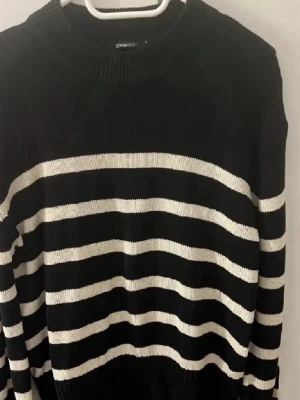 Svartvit randig stickad tröja Gina Tricot - Säljer en svart stickad tröja från Gina Tricot med vita horisontella ränder. Tröjan har rund halsringning och långa ärmar. Perfekt för dig som gillar klassiska mönster och enkel stil.