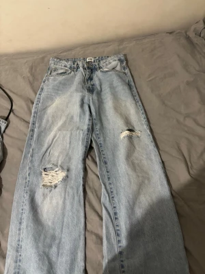 Ljusa slitna jeans från lager 157 - Säljer ett par ljusblå jeans från lager157 med raka ben och slitningar på båda benen. Jeansen har klassisk femficksdesign och hög midja. Perfekta för en avslappnad och trendig look.