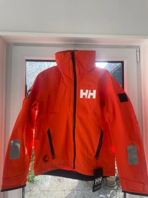 Helly Hansen jacka - En sprillans ny Helly Hansen seglar/vindjacka. Jackan har även en inbyggd luva som är enkel att fälla in och ut. Materialet är slitstarkt och vattenavvisande, perfekt för blåsiga dagar. Jackan kostar 2200kr från butik och nätet.        Pris går att diskutera 