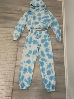 Blåvit tie dye loungewear-set - Säljer ett par mjukisbyxor och hoodie i blåvitt tie dye-mönster med resår i midja och benslut. Sköna och avslappnade med en riktigt chill vibe, perfekta för att hänga hemma eller dra ut på stan. Matchar snyggt med hoodie i samma stil. Materialet är mjukt bomullstyg. Inga fläckar eller hål vad jag kunnat se vid syning 