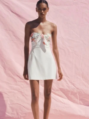 Vit axelbandslös kortklänning med blommigt liv - Söt axelbandslös kortklänning med vit kjol och blommigt liv i pastellfärger. Klänningen har en knytdetalj framtill och en figurnära passform. Perfekt för sommarens varma dagar.