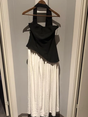 Balklänning från babyboo - Svart och ch vit balklänning från babyboo. Tillkommer en svart scarf. Klänningen har en vit flowig underdel med slits och en tajt överdel med korsett som knytning. Andvänd endast en gång 