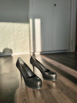 Svarta klassiska pumps med hög klack från Yves Saint Laurent, Storlek 40 - Säljer ett par svarta pumps med rund tå och hög smal klack. Skorna har en stilren och tidlös design med slät yta och lätt platå framtill. Perfekta för dig som vill ha ett par eleganta klackar till garderoben.