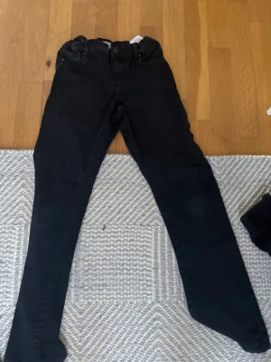 Svarta  jeans - Säljer ett par svarta skinny jeans med hög midja och klassisk femficksdesign. Jeansen har smal passform och är tillverkade i stretchigt material för extra komfort. Perfekta till en avslappnad eller trendig look.