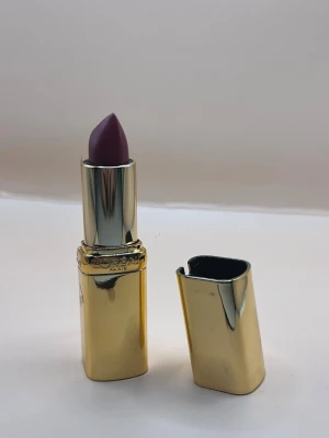 Lila läppstift från L'Oréal Paris - Snyggt lila läppstift från L'Oréal Paris med elegant guldfärgat hölje. Läppstiftet har en klassisk rundad form och känns lyxigt att ha i väskan. Perfekt för dig som vill ha en djup, trendig färg på läpparna.